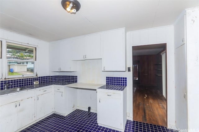 kitchen with tasteful backsplash, wooden walls, white cabinetry, and a sink