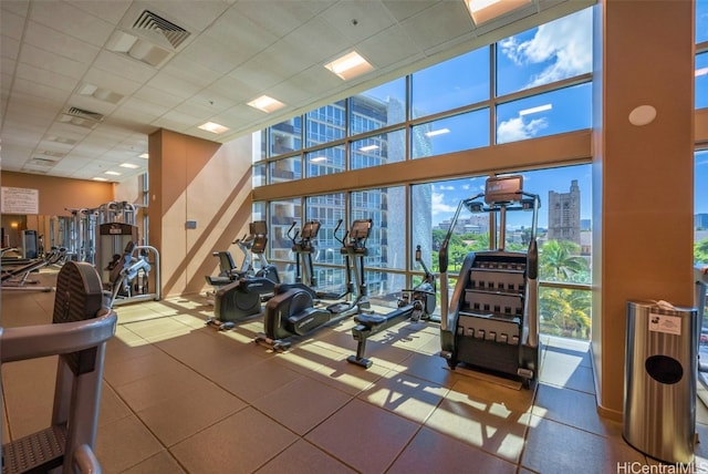 exercise room with a wall of windows, a view of city, visible vents, and a paneled ceiling