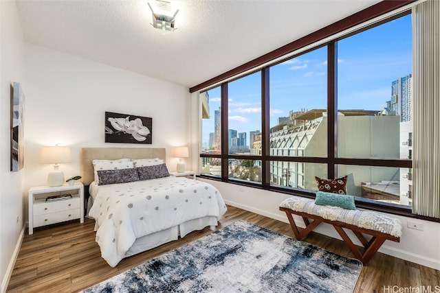 bedroom with baseboards, a textured ceiling, wood finished floors, and a city view