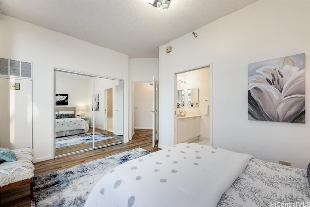 bedroom with a closet, visible vents, connected bathroom, a textured ceiling, and wood finished floors