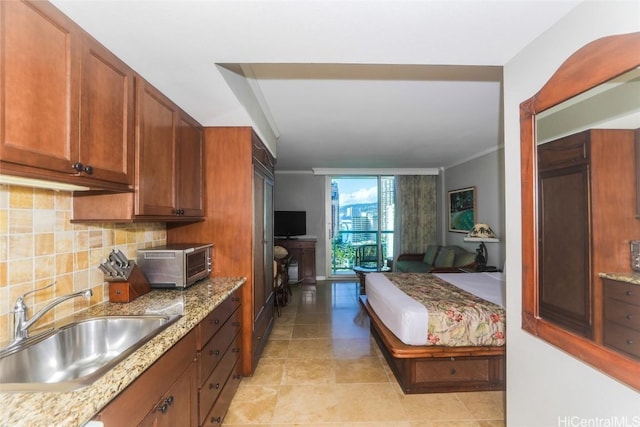 kitchen featuring a toaster, decorative backsplash, brown cabinetry, light stone countertops, and a sink