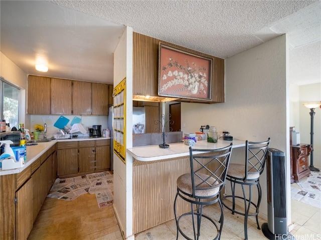 kitchen with light countertops, a peninsula, a kitchen bar, and brown cabinets