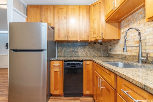 kitchen with dishwasher, light stone counters, freestanding refrigerator, light wood-type flooring, and a sink