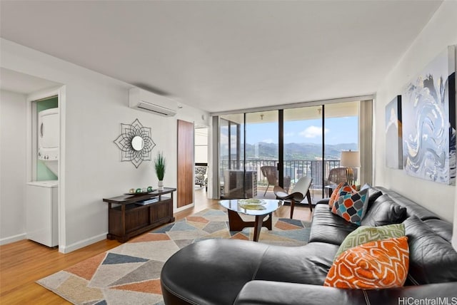 living room with floor to ceiling windows, stacked washer / dryer, an AC wall unit, a mountain view, and light wood-type flooring