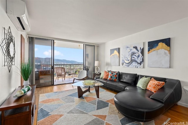 living room featuring a wall mounted air conditioner, wood finished floors, a mountain view, a wall of windows, and baseboards