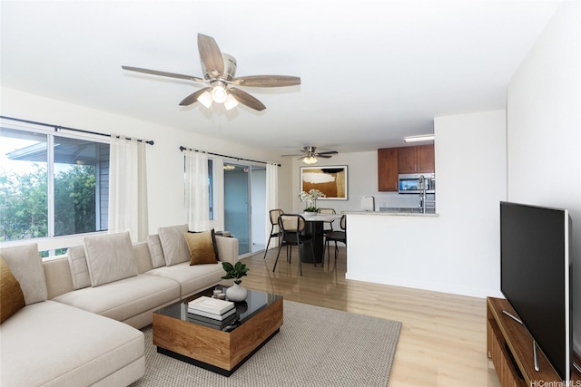 living room with baseboards, a ceiling fan, and light wood-style flooring