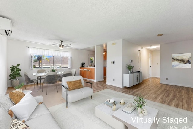 living area with wood finished floors, ceiling fan, a textured ceiling, and a wall mounted AC