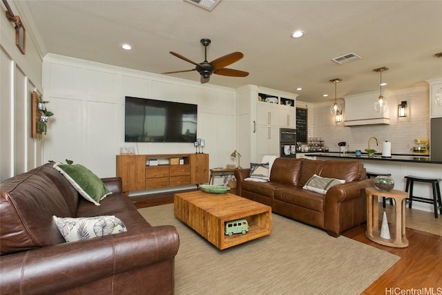 living room with recessed lighting, visible vents, a decorative wall, ornamental molding, and wood finished floors