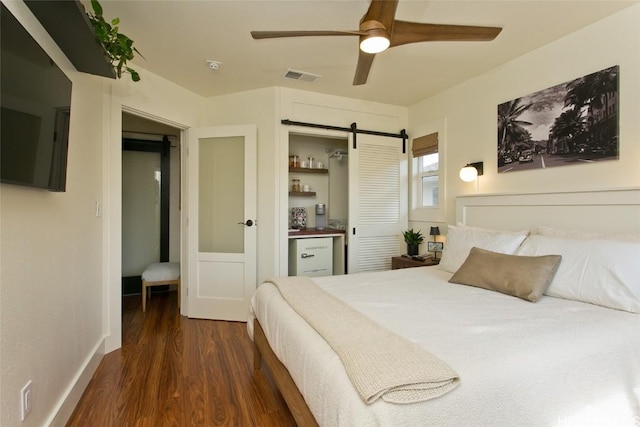 bedroom featuring dark wood finished floors, visible vents, a barn door, ceiling fan, and baseboards