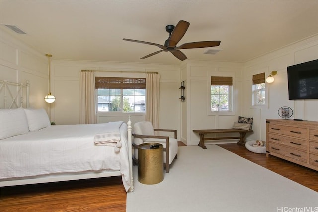 bedroom featuring a decorative wall, wood finished floors, visible vents, and crown molding