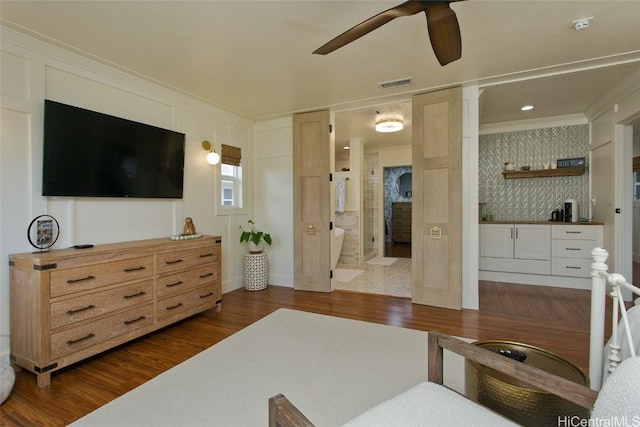 living room with dark wood-style floors, ceiling fan, visible vents, and crown molding