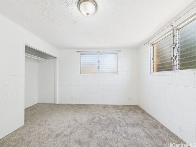 spare room featuring carpet floors, concrete block wall, and a textured ceiling