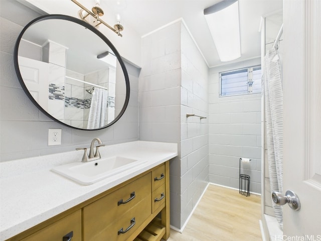 full bathroom with a shower with shower curtain, tile walls, wood finished floors, and vanity