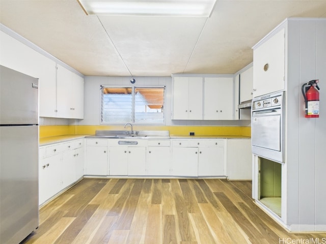 kitchen with white cabinetry, light countertops, white oven, light wood-type flooring, and freestanding refrigerator