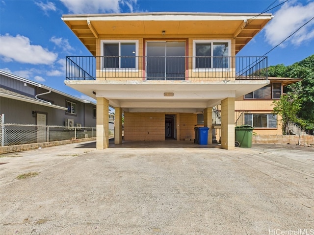 view of front of house with a carport, driveway, a balcony, and fence