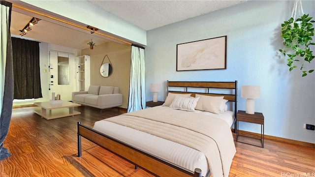 bedroom with track lighting, a textured ceiling, baseboards, and wood finished floors