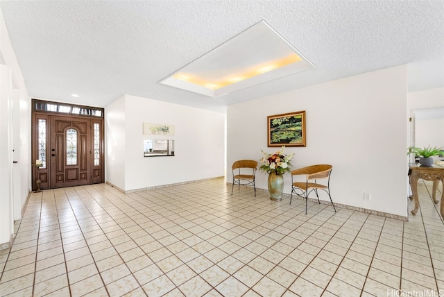 entrance foyer featuring a tray ceiling, a textured ceiling, baseboards, and light tile patterned floors