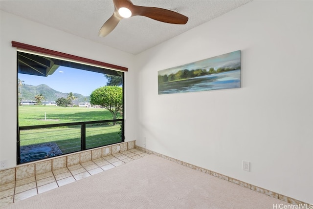 unfurnished room with carpet, a mountain view, a textured ceiling, ceiling fan, and tile patterned flooring