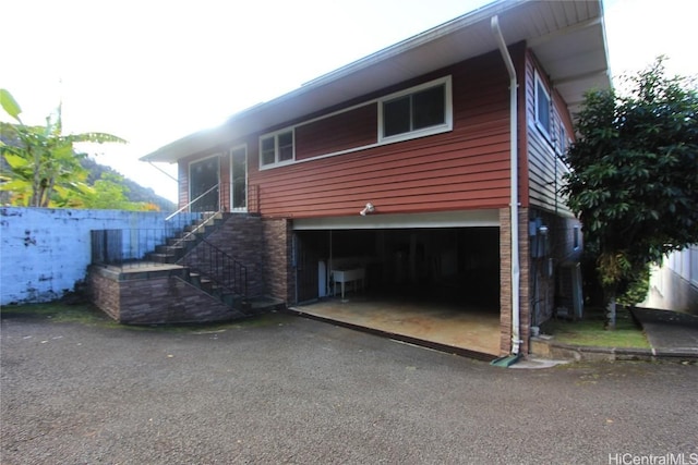 exterior space featuring stairway, aphalt driveway, an attached garage, fence, and brick siding