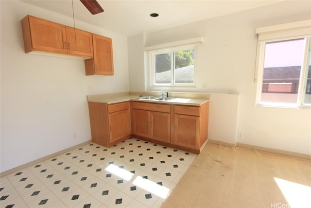 kitchen featuring a sink, a ceiling fan, baseboards, light countertops, and brown cabinets