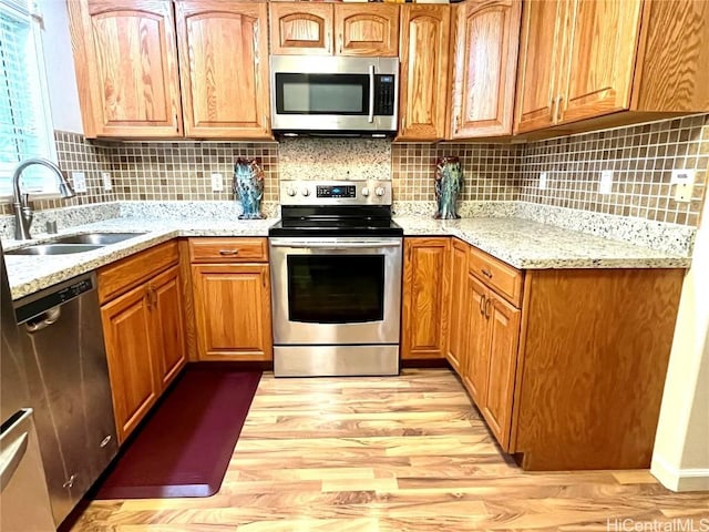 kitchen featuring backsplash, appliances with stainless steel finishes, light wood-style floors, a sink, and light stone countertops