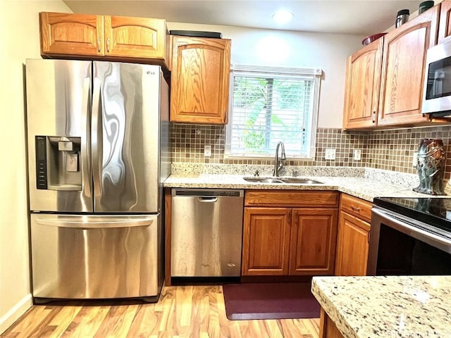 kitchen with light stone counters, stainless steel appliances, light wood-style flooring, decorative backsplash, and a sink