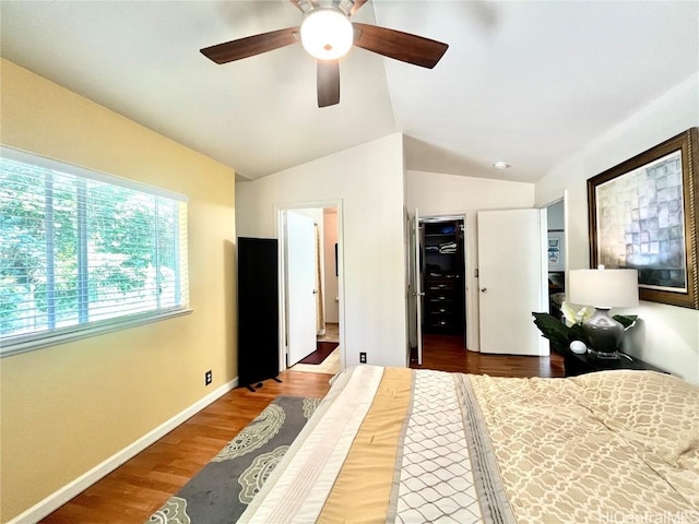 bedroom with a spacious closet, ceiling fan, vaulted ceiling, wood finished floors, and baseboards