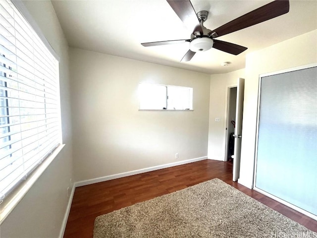 unfurnished bedroom with dark wood-type flooring, a closet, baseboards, and a ceiling fan