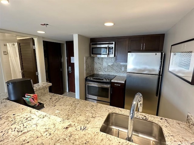 kitchen with dark brown cabinetry, decorative backsplash, light stone counters, stainless steel appliances, and a sink