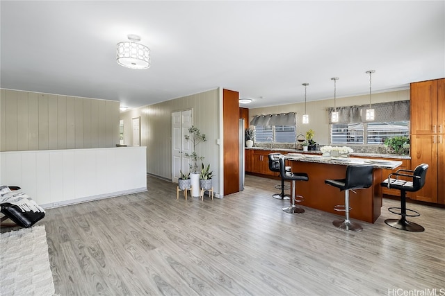 kitchen with a breakfast bar, a kitchen island, light wood-style floors, brown cabinetry, and decorative light fixtures