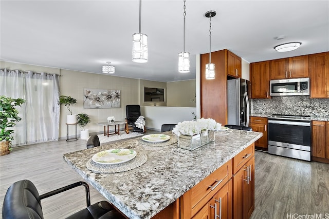 kitchen with light stone counters, a center island, brown cabinets, stainless steel appliances, and open floor plan