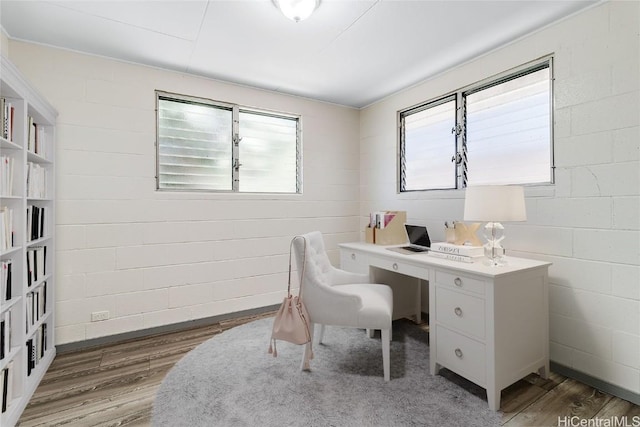 home office with concrete block wall and wood finished floors