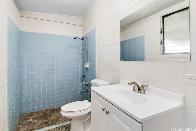 bathroom featuring tile walls, tiled shower, vanity, and toilet