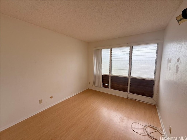 spare room featuring a textured ceiling, light wood-style flooring, and baseboards