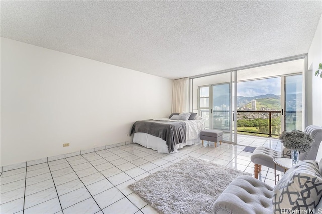 bedroom with a textured ceiling, light tile patterned flooring, a mountain view, access to outside, and expansive windows