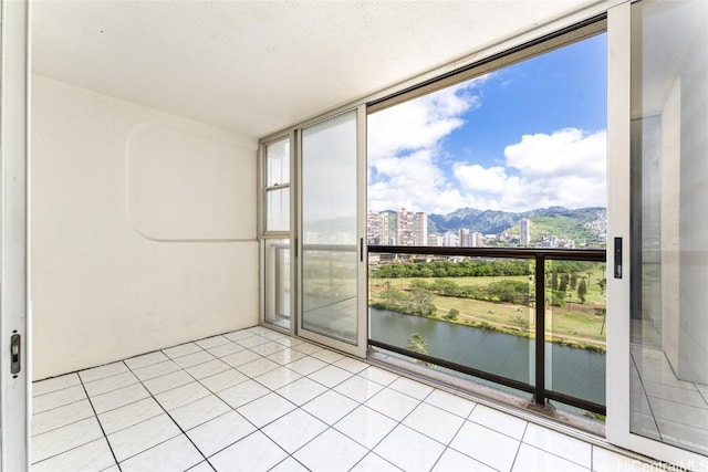 empty room featuring a city view, light tile patterned floors, a water view, expansive windows, and a textured ceiling