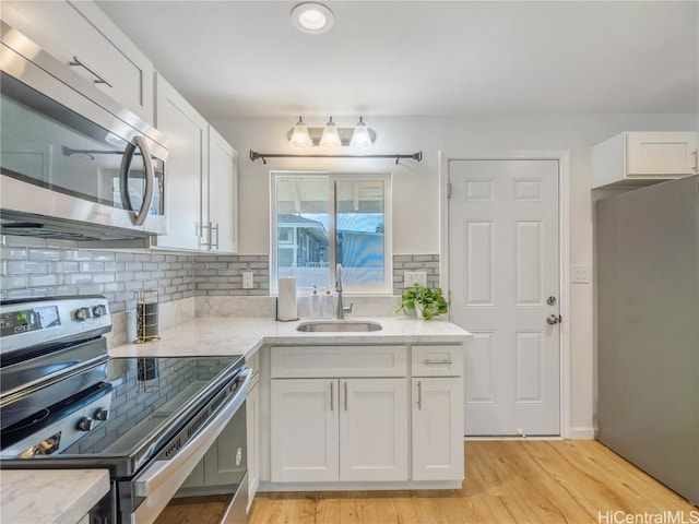 kitchen featuring appliances with stainless steel finishes, a sink, light wood-style floors, and white cabinets