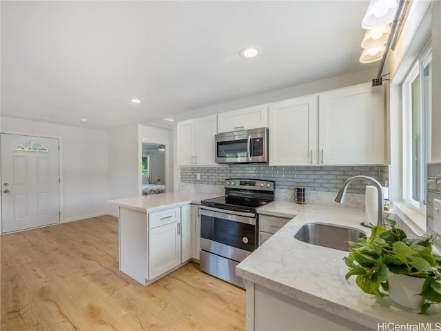 kitchen featuring stainless steel appliances, a peninsula, a sink, white cabinets, and light wood-type flooring