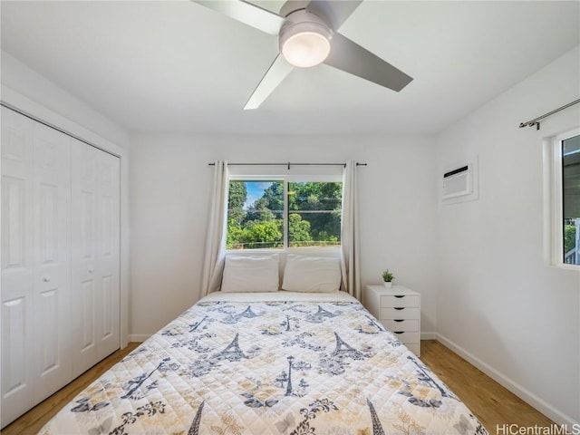 bedroom with ceiling fan, a wall unit AC, wood finished floors, baseboards, and a closet