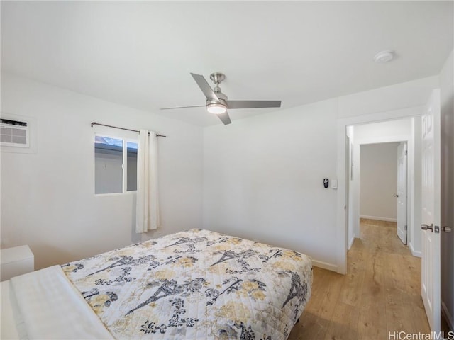 bedroom with light wood finished floors, a wall unit AC, a ceiling fan, and baseboards