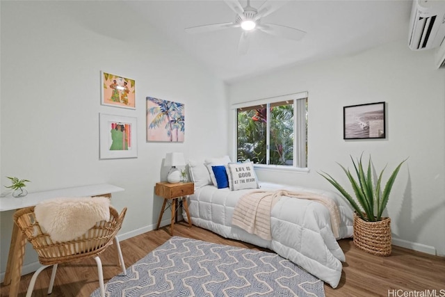 bedroom with lofted ceiling, ceiling fan, a wall unit AC, wood finished floors, and baseboards