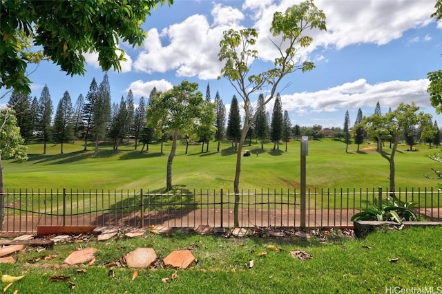 view of community featuring view of golf course, a lawn, and fence