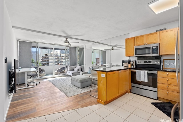 kitchen with appliances with stainless steel finishes, dark countertops, open floor plan, and a peninsula