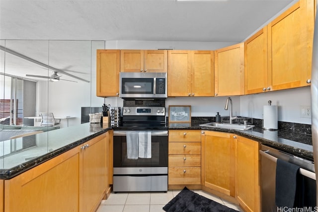 kitchen featuring light tile patterned floors, dark stone counters, stainless steel appliances, and a sink