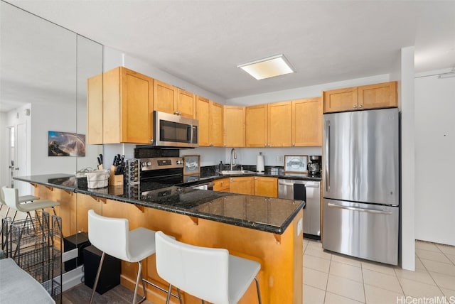 kitchen with a breakfast bar, dark stone countertops, a peninsula, stainless steel appliances, and a sink