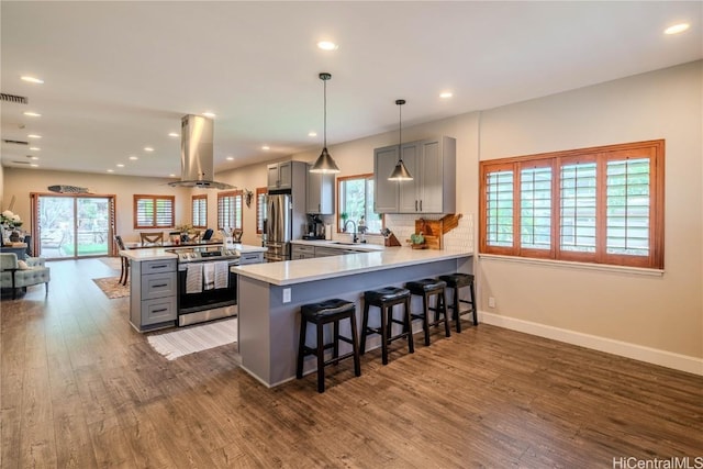 kitchen with gray cabinetry, island range hood, stainless steel appliances, a peninsula, and hanging light fixtures