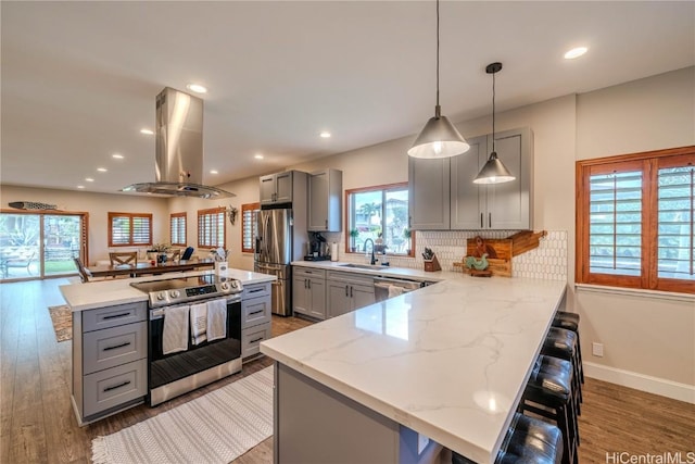 kitchen with a breakfast bar, decorative light fixtures, island exhaust hood, gray cabinetry, and appliances with stainless steel finishes