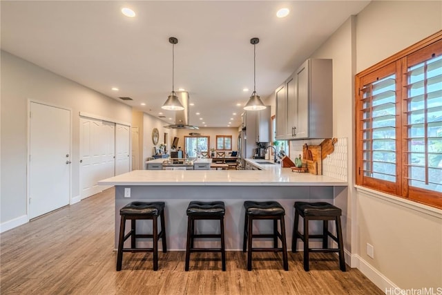 kitchen with a peninsula, light wood-style floors, light countertops, gray cabinets, and pendant lighting