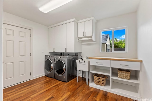 clothes washing area featuring wood finished floors, washing machine and clothes dryer, cabinet space, and baseboards