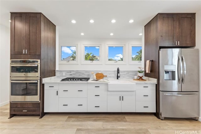 kitchen featuring light stone counters, stainless steel appliances, decorative backsplash, white cabinets, and a sink